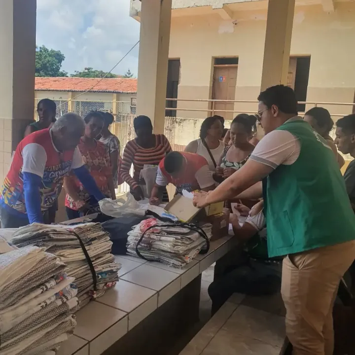 Voluntária da Devoluto, de colete verde, e moradores organizando papelão numa mesa comprida, durante o Carnaval Sustentável de 2023 em Olinda.