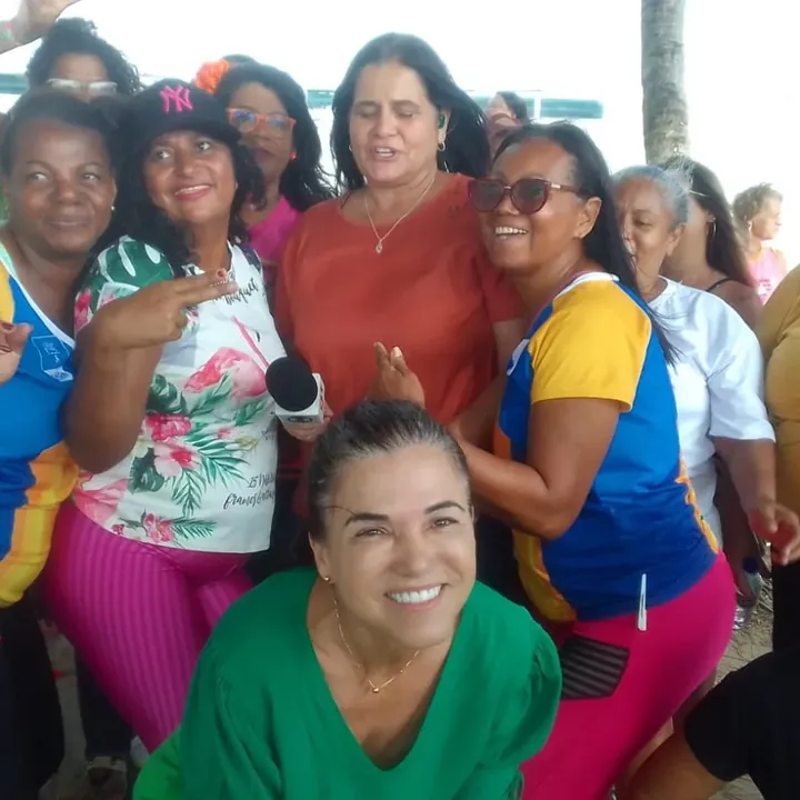 Grupo de mulheres sorrindo, uma delas segurando um microfone, em comemoração ao Dia Internacional da Mulher.