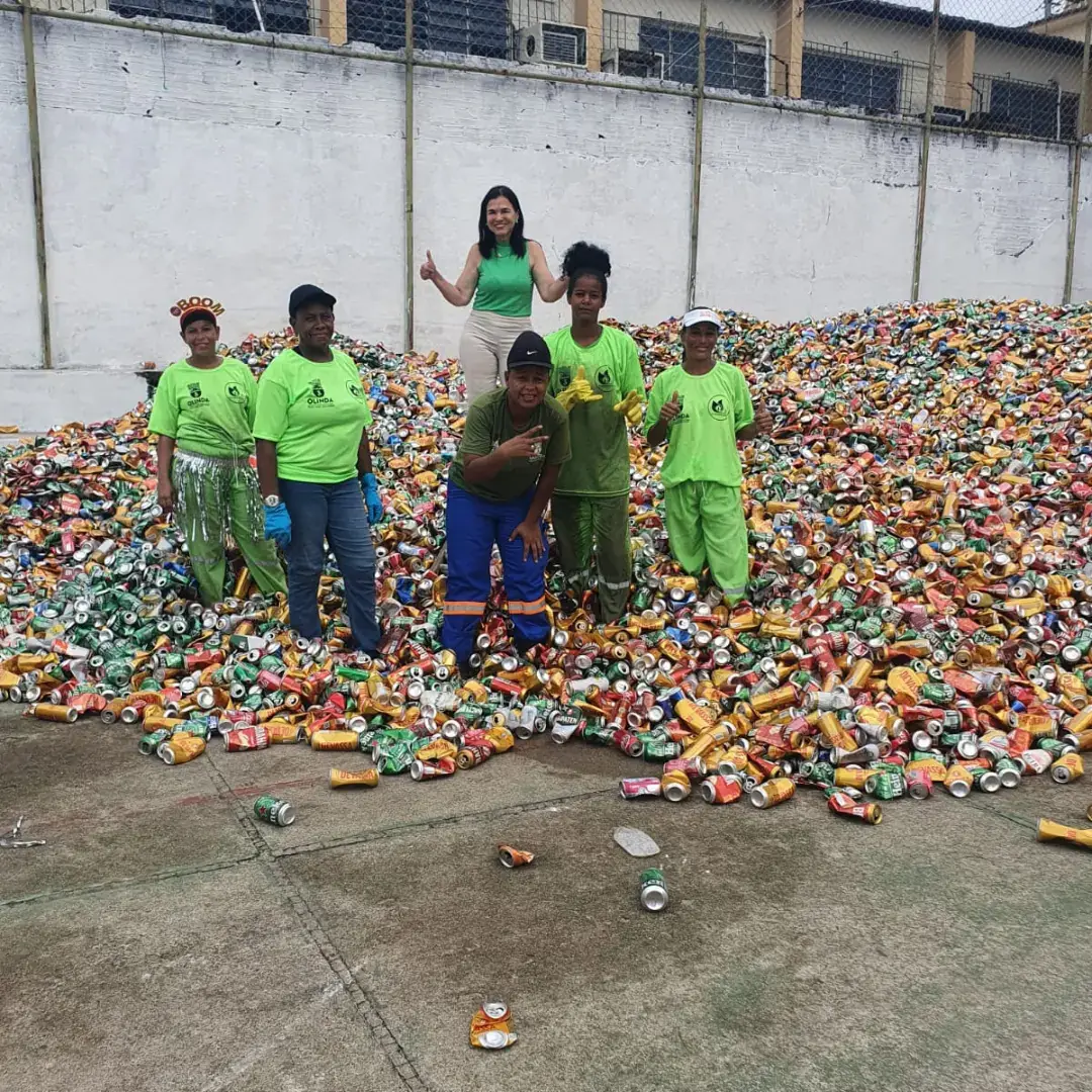 Agentes da reciclagem de camiseta verde sobre uma montanha de latas, no Carnaval Sustentável de 2023 em Olinda.